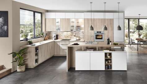 Helle, moderne Küche mit einer Kombination aus Holz- und Weißschränken, einer Kücheninsel und großen Fenstern mit Blick auf einen Garten.